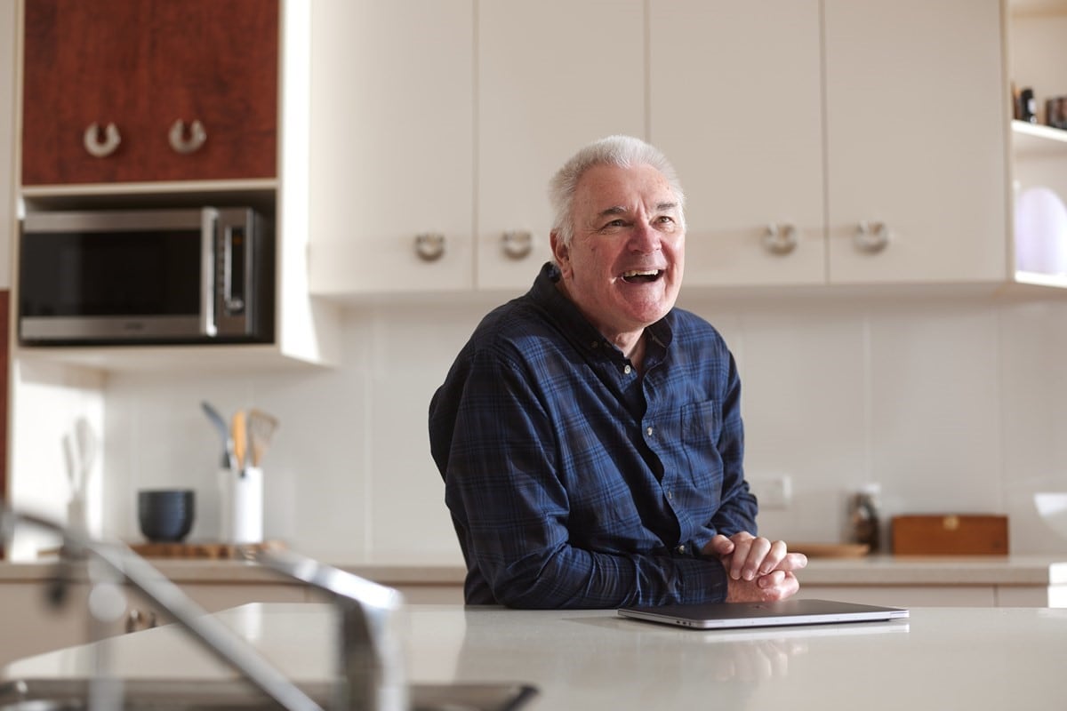 Geoff, VPP customer, leaning against kitchen bench smiling
