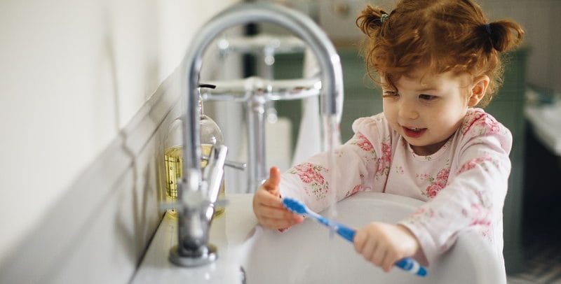 Young girl running water while brushing her teeth