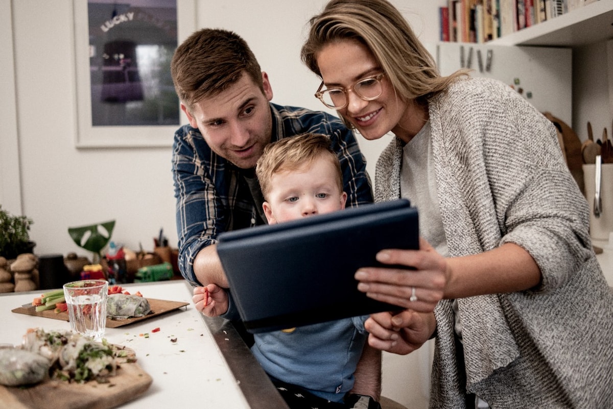 A mother, father and toddler sitting at the kitchen counter looking at an iPad