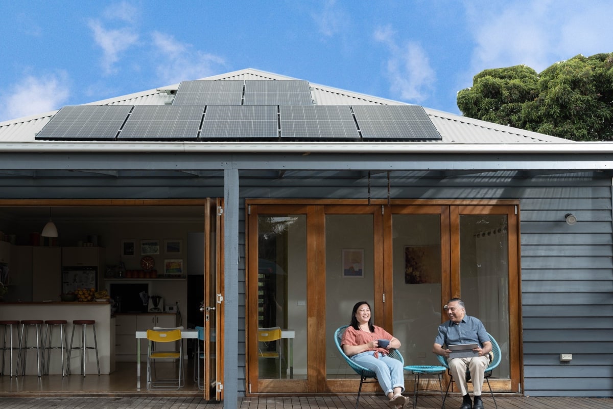 Two people sitting on a verandah beneath their rooftop solar panels.