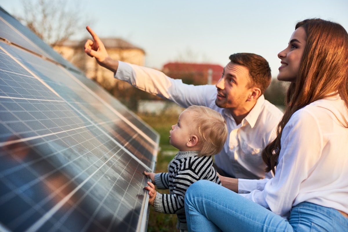 Young family of three crouching in front of a solar panel looking up