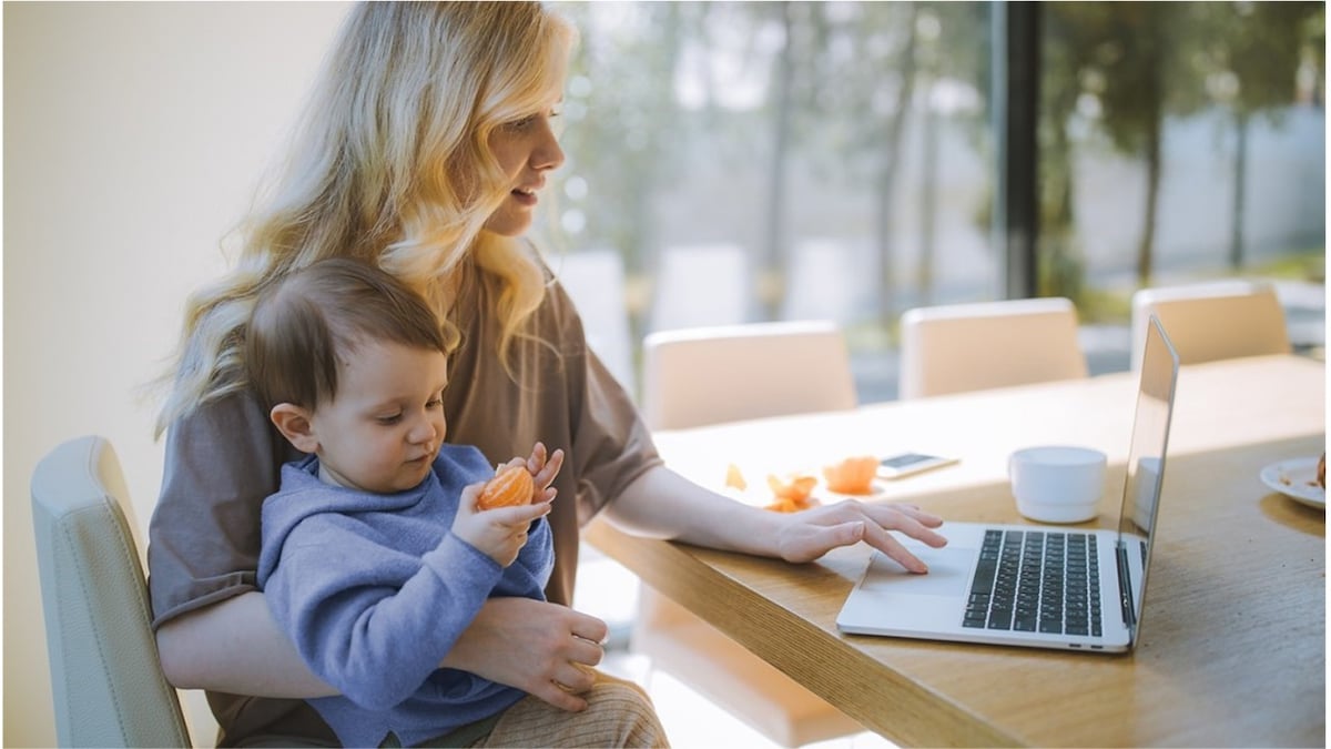 Woman holding a little boy while working on a laptop