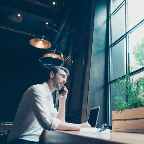 A man sitting at an office desk, talking on a mobile phone and looking out the window
